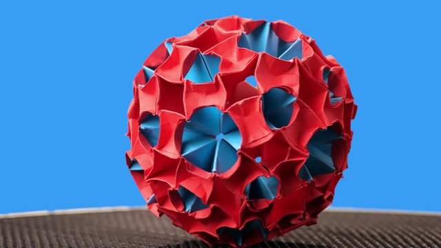 Red and blue origami magic ball model. Sphere rotation. Blue background.