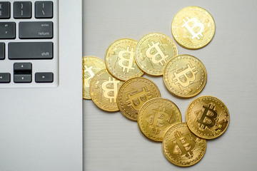 Gold bitcoins appearing from above the side of silver laptop
