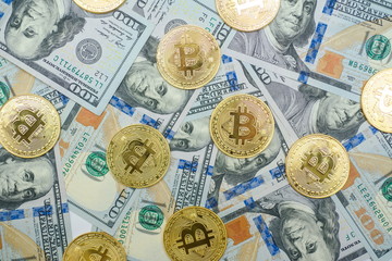 A bunch of gold bitcoin coins laying over hundred dollar bills background 