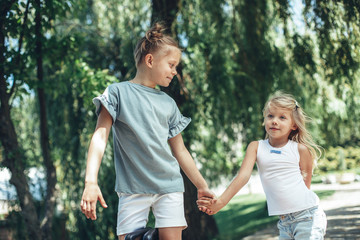 Fototapeta premium Full length of delighted girl holding sister hand outside. They are strolling outdoors with delight enjoying summer time