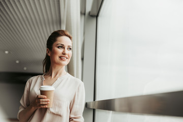 Portrait of beaming girl tasting mug of beverage while resting indoor at job