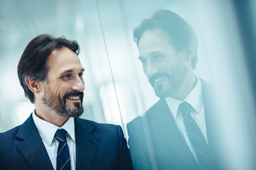 Side view beaming unshaven man in contemporary suit watching at reflection