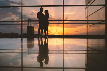 Full length side view smiling male hugging outgoing woman opposite beautiful sunset in airport. Glad lovers before journey concept