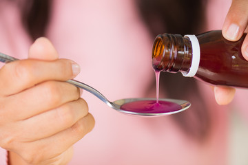 Woman hand pouring medication or antipyretic syrup from bottle to spoon. healthcare, people and...