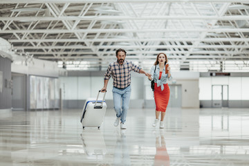 Full length portrait of worried male and woman running with baggage indoor. They late for flight