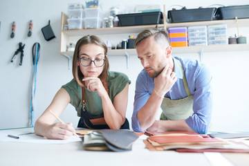 Fototapeta premium Two tailors thinking about the new goods from leather at the workplace. They drawing sketch