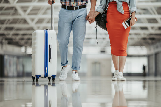 Close up male and woman legs. He holding luggage while keeping female arm. Travel concept