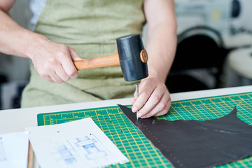 Close-up of male master working with hammer and piece of leather at the table