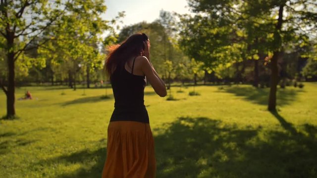 Beautiful redhead female with long hair enjoys music with headphones, running in the park. She jumping like in childhood.