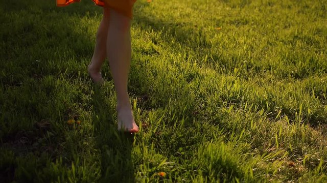 Female's feet running by grass in park. No face. Sunset or surise. Super slow motion. Middle skirt, slender legs, barefoot. Front view close-up.