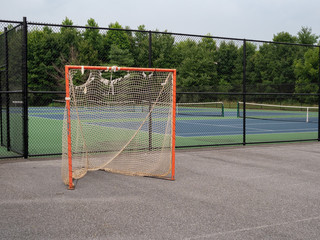 Offseason, beat up, rusted, ragged lacrosse goal sitting on asphalt court with nets tearing