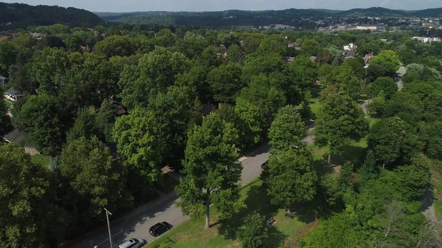 A rising aerial establishing shot of the residential district of a small town in western Pennsylvania on a summer day. Pittsburgh suburbs.  	