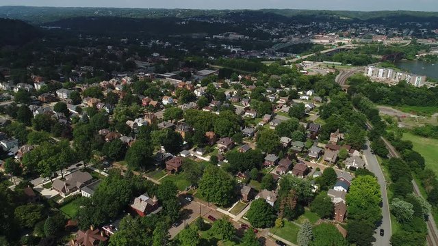 A slow reverse aerial establishing shot of the residential district of a small town in western Pennsylvania on a summer day. Pittsburgh suburbs.  	
