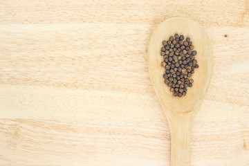 peppercorns in spoon heap on wooden table.