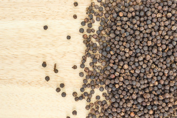 black peppercorns heap top view on wooden background.