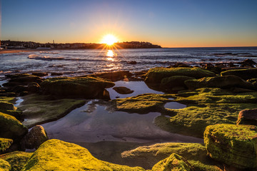 Sun rising over ocean and rocky coastline with blue sky