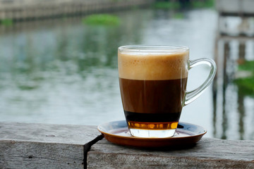 Special recipe hot coffee with milk on top and syrup in clear coffee cup served in a shop beside the river in a relax time with space for write wording, good environment for meet friend or lovers