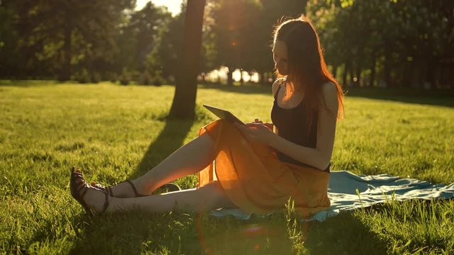 Young lady using tablet computer outdoors. Stabilizer smooth shot of typing and Internet surfing using digital pad. Sunset lighting.