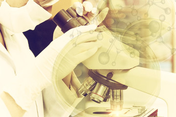 Sepia style picture of scientist looking through a microscope in a laboratory. she is doing some research