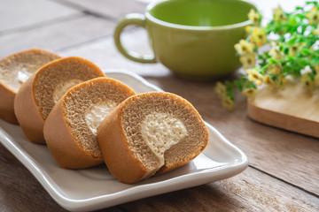 Coffee roll cake with cream on plate and coffee cup