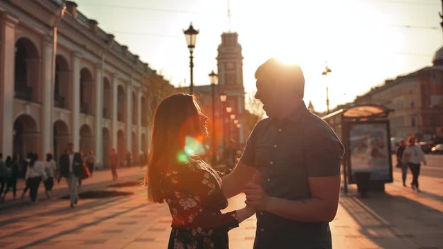 A beautiful couple dancing an dance with elements of waltz, leaks of sun. City background with cars and transport. blurred people. 4k ultra hd slow motion. Sunset or sunrise