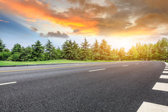 Asphalt road and green forest landscape at sunset