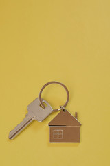 Key chain with silver house shaped pendant on yellow background closeup top view with copy space for text. Real estate, buying and moving new home or renting property or apartments concept.
