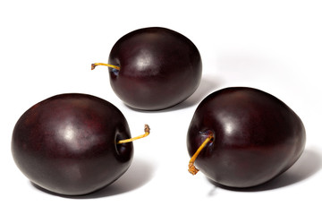 Three ripe black plums on a white background