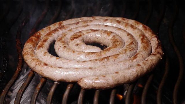 Slow motion shot of the delicious homemade meat sausage frying on the grill with flames and smoke
