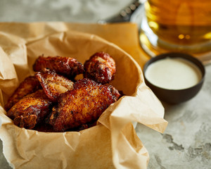 Close-up view of bowl with fried chicken wings,  served with sauces and glass of beer