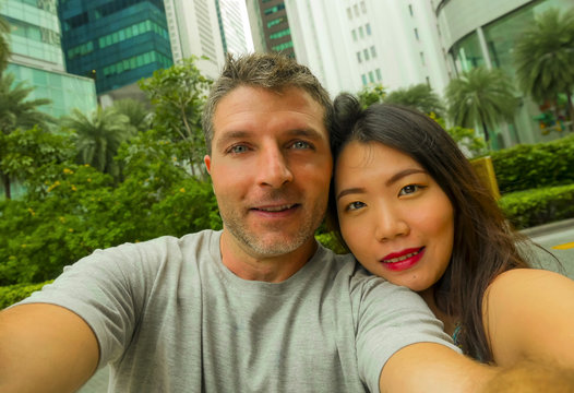 young happy and attractive mixed Asian Caucasian ethnicity couple in love taking selfie picture together smiling cheerful enjoying holidays travel