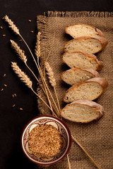 Pieces of sliced ​​baguette lie on a dark jute napkin.  Nearby lie a few spikelets of wheat