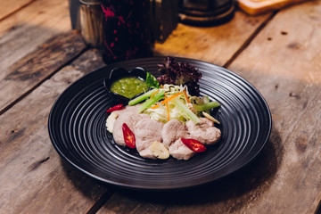 Thai steaming pork served with spicy sauce in black circle plate.