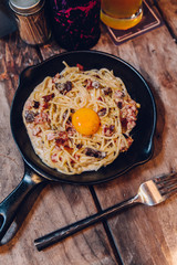 Fettuccine Carbonara yolk bacon served in black pan on wooden table.