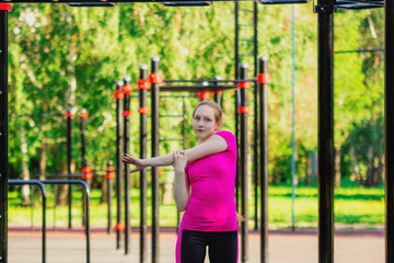 Shoulder stretching warm up. Girl in pink sportswear doing exercises at street workout place in summer morning. Healthy lifestyle sport concept.