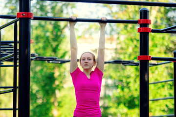 Fototapeta premium Pull ups on a horizontal bar. Girl in pink sportswear doing exercises at street workout place in summer morning. Healthy lifestyle sport concept.