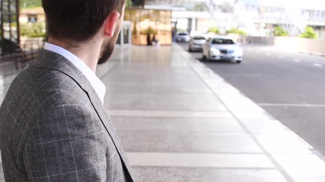 Businessman stands near Parking and looks at clock waiting for taxi