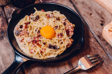 Fettuccine Carbonara yolk bacon served in black pan on wooden table.