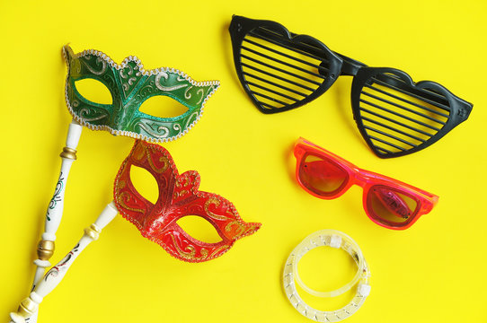 Carnival venetian masks in green and red with handle, fancy glasses and glitter bracelets for photo booth isolated on vibrant yellow background, Fancy mask with copy space