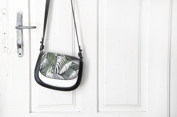 handbag with palm motif hung on old white door