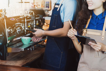 Man barista & Woman barista wear apron holding notepad and get order on counter bar served to customer in coffee shop.Concept of cafe and coffee shop small business.Vintage tone