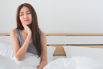 Young Asian woman feel toothache and discomfort on bed in white bedroom morning.Concept of women's health care.
