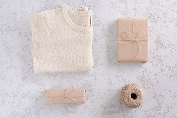 Brown kraft gift box, knitted sweater, jute rope on white textured table, top view and flat lay