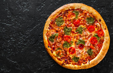 Pizza with Mozzarella cheese, Ham, Tomatoes, pepper, Spices and Fresh Basil pesto sauce. Italian pizza.on black background. with copy space. top view