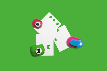 three small colored plastic hole punchers with sheets of paper standing on the green background. concept of office chancery. free space for text