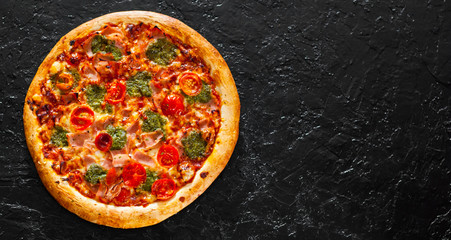 Pizza with Mozzarella cheese, Ham, Tomatoes, pepper, Spices and Fresh Basil pesto sauce. Italian pizza.on black background. with copy space. top view