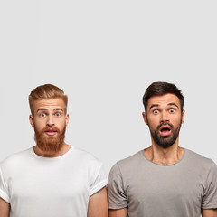 Vertical shot of surprised two men with thick stubble, wonder latest news about friend, open eyes...