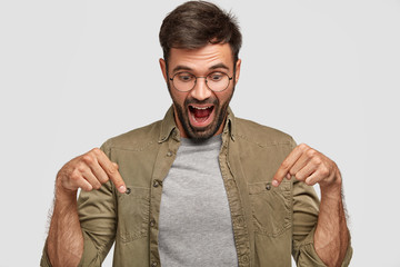 Wow, that`s amazing! Amazed shocked young male looks with surprisement down, points with both index...