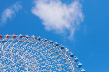 Large ferris wheel revolves around a circle with a blue sky as the background.