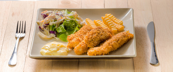 Deep fried fish steak served with french fries and fresh vegetables on white plate.